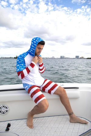 A man on the back of a boat with a hooded long sleeve top and bathing suit